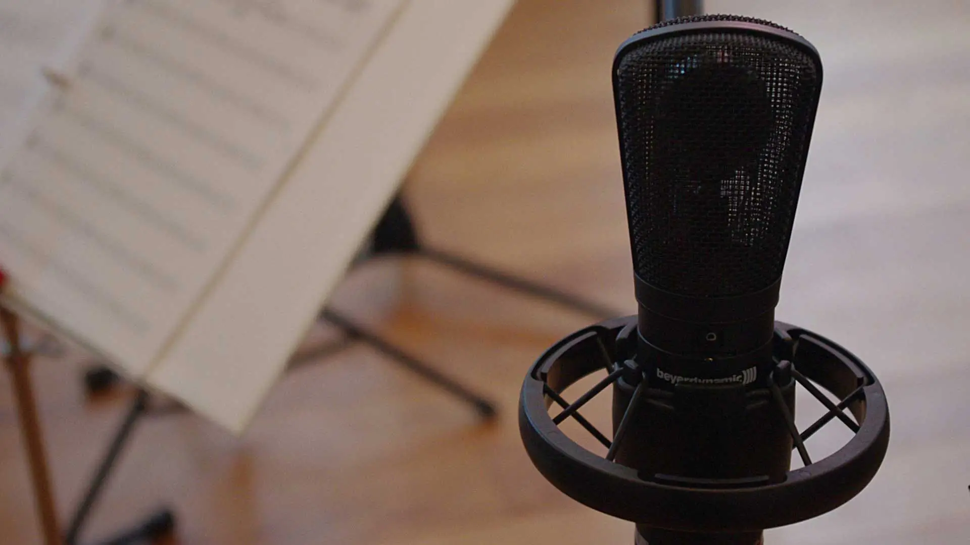 Close-up of a microphone with a blurred music stand in the background.