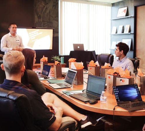 A typical office boardroom with people sat around a desk with computers on it to show corporate voice over demo samples are available to hear