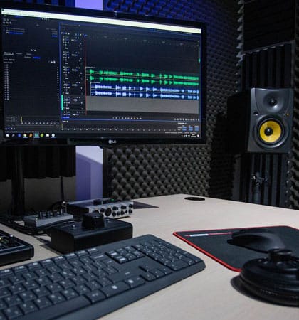 A modern audio editing workstation with dual monitors, speakers, and soundproofing foam.