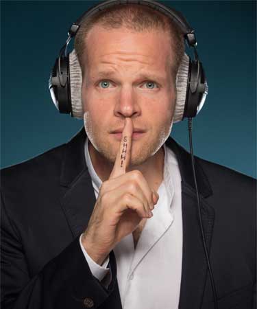 Neil Williams English Male Voiceover Artist wearing a suit and headphones with his right hand to his mouth and the words shhhh written on them