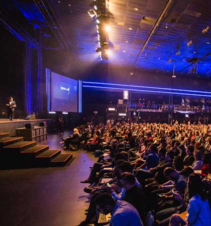 an arena packed with people sat on chairs watching a presentation on stage the voiceover being used to introduce the show could be one by Neil Williams Male Voiceover Artist