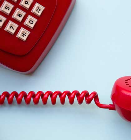 a red phone with push buttons and old style coiled cord being used to represent on hold voiceovers you might hear on the telephone