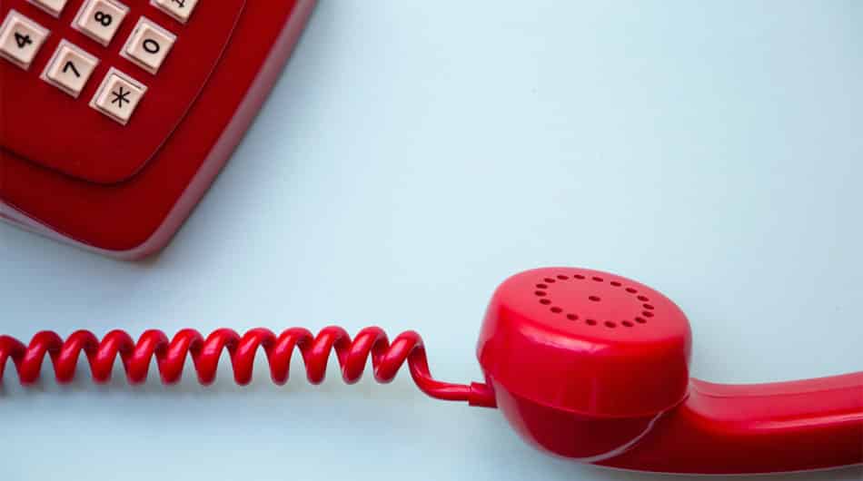 the corner of a red phone, old school with push buttons, it also has a curled chord leading to the red handset to show the on hold messaging voice voers neil williams has recorded for clients around the world.