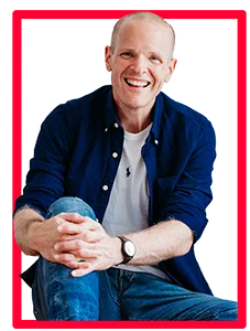 neil williams british male voice over artist who offers free voice over demo examples. The photo shows him in a blue shirt and white tshirt, with his arms around his right leg, smiling at the camera.